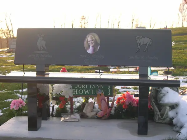A polished dark granite memorial bench with a full back panel carrying three names, each with an etched image, and a name cut along the seat edge