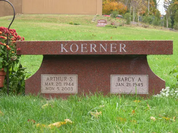 A red granite memorial bench with the surname cut across the seat edge and two name tablets set into the solid base