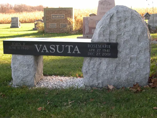A grey granite memorial bench paired with a rough-hewn granite boulder, the surname and two names cut along the seat edge