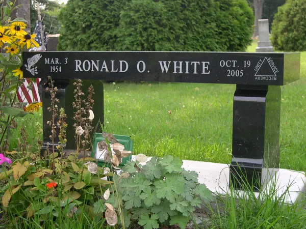 A polished black granite memorial bench with a name and two dates cut along the seat edge and a service emblem at one end