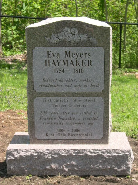A grey granite historical monument with a rounded top and carved flowers, recording the first burial in a pioneer cemetery and marking the Kent, Ohio bicentennial