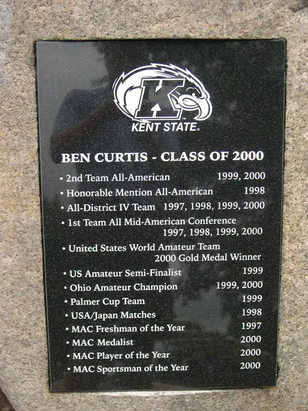 A polished black granite plaque set into granite, carrying a university athletics emblem and a list of a golfer's collegiate honours by year