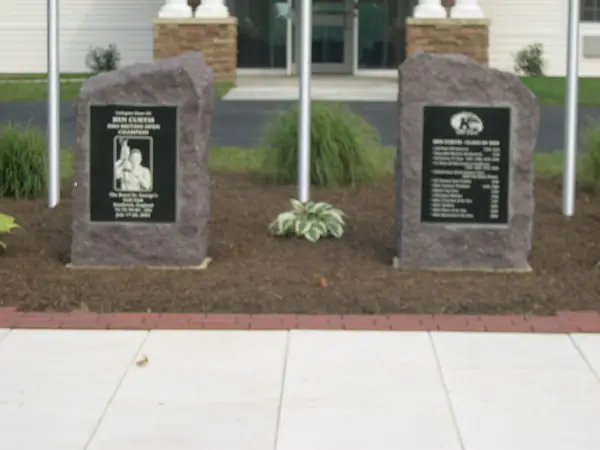 Two rough-hewn granite boulders with polished black plaques set either side of a flagpole outside a modern building