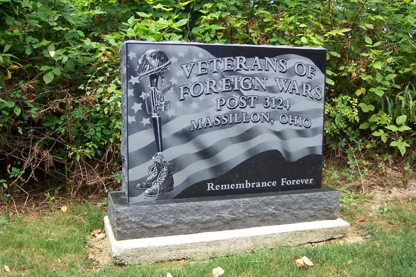 A polished black granite VFW post memorial etched with an American flag, a battlefield cross of rifle, helmet and boots, and the post number and town, Massillon, Ohio