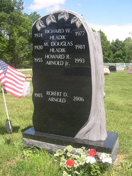 A polished black granite monument shaped as a tree trunk with a carved bark edge and laurel branches, carrying four names and their years