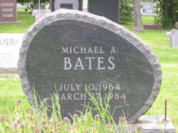 An oval dark grey granite monument with a rounded top, carrying the full name and dates in raised lettering