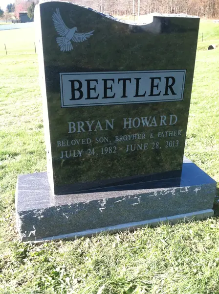 A polished black granite monument with an asymmetric wave-cut top, an etched dove, a raised name panel and a relationship line above the dates