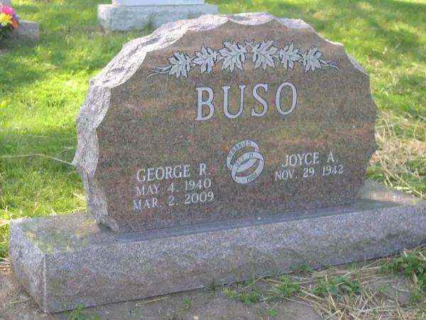 A grey granite monument with a rounded top and a carved band of oak leaves, two name tablets and a wedding-ring emblem between them