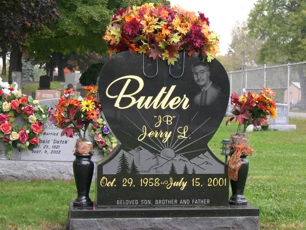 A heart-shaped polished black granite monument with an etched portrait, the family name in gold script and an etched mountain sunrise below