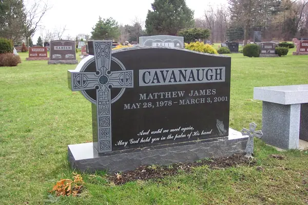 A polished black granite monument with a full-height Celtic cross carved at one side, the name and dates beside it and an epitaph in script below