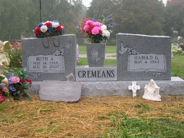 A pair of grey granite tablets set on one base either side of a granite vase, each carved with doves and butterflies, with the family name across the base