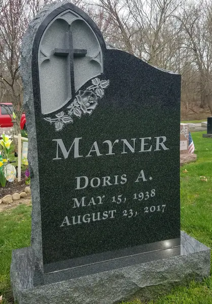 A polished dark granite monument with an arched Gothic niche carving containing a cross and lilies, and the name and dates in cut lettering