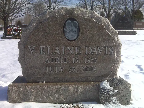 A grey granite monument with a rough-hewn top and side edges, a recessed oval portrait and the full name and dates in cut lettering