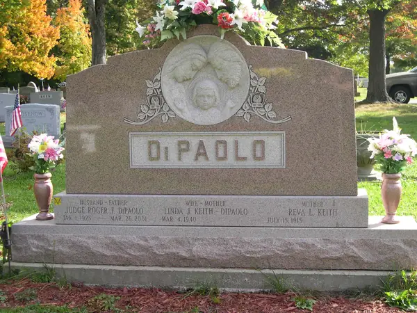 A rose granite monument with a carved cherub medallion above a raised name panel, and three name tablets labelled by relationship