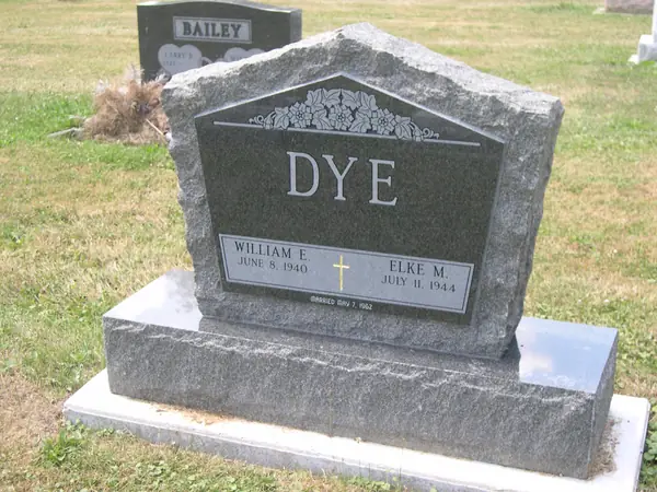 A grey granite monument with a peaked, gabled top carved with flowers, two name tablets, a gilt cross between them and a marriage date below
