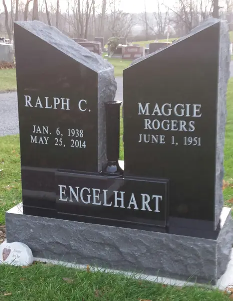 A polished black granite monument built as two open book pages standing apart, each carrying a name, with the family name on a raised panel across the base