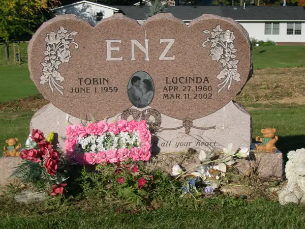 A rose granite monument with a double-heart top, carved floral corners, an etched oval portrait between two names and an epitaph in script