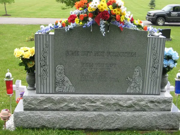 A grey granite monument with an epitaph across the top, a verse in the centre and figures of Christ and the Virgin Mary carved at the lower corners