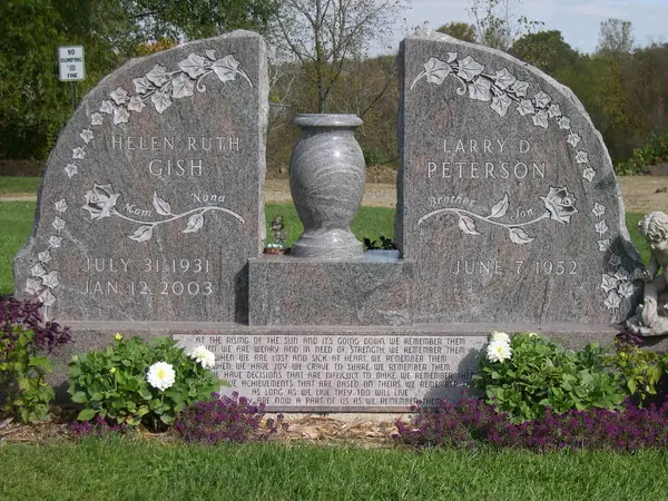 A rose granite double monument of two shaped tablets flanking a granite vase, each carved with ivy and a rose, with a long verse cut across the base