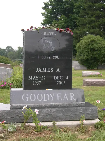 A dark grey granite monument with an oval etched motorcycle scene, a nickname above it, a short epitaph and the family name cut into the base