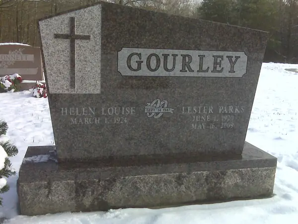 A rose granite monument with an angled top and a full-height carved cross, a raised name panel and a marriage emblem between the two names
