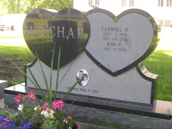 A monument built from two joined granite hearts, one polished black and one light grey, carrying the family name, two names, a small portrait and a marriage date