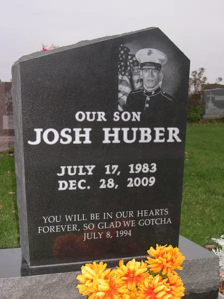 A polished black granite monument with an angled top, an etched portrait of a serviceman in dress uniform beside a flag, a relationship line and a short epitaph