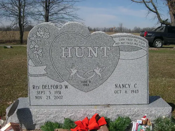 A grey granite monument with a large carved heart at its centre, doves and a wedding-ring emblem inside it, roses at one shoulder and a scroll epitaph at the other