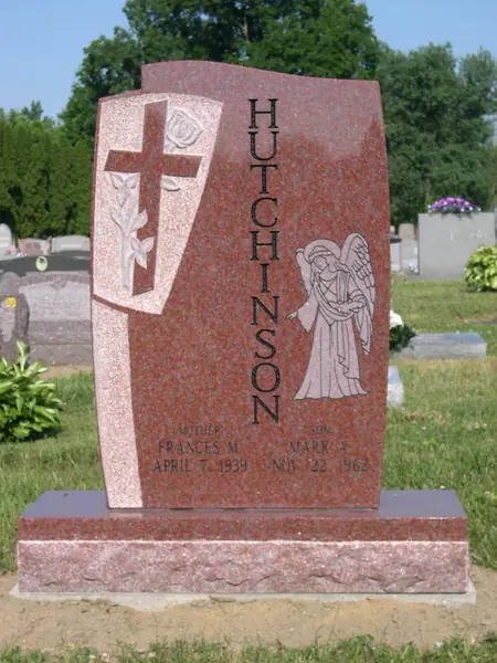 A red granite monument with a wave-cut top, a carved cross and dove on a draped banner, an angel carved at the other side and the family name set vertically