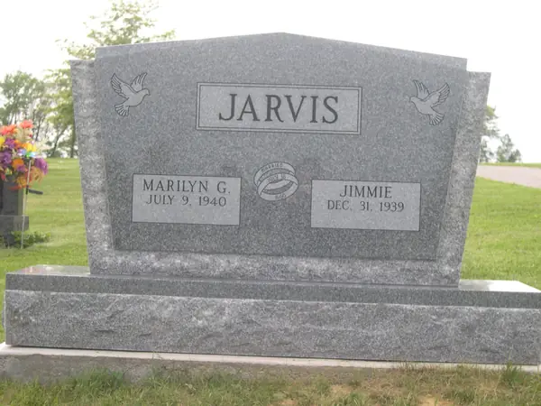 A light grey granite monument with doves carved at both upper corners, a raised name panel and a wedding-ring emblem between the two name tablets