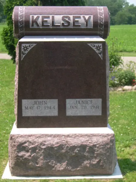 A two-tone monument with a polished black granite face and a rose granite cap and base, carved corners and two raised name tablets