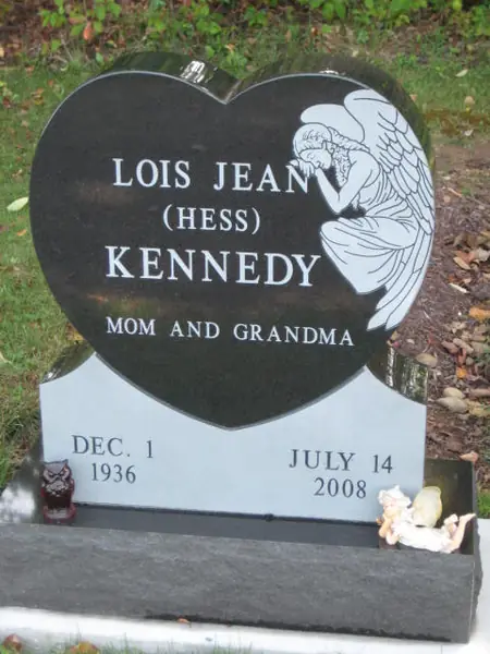 A monument built from a polished black granite heart carved with an angel, set on a light grey granite base carrying the dates