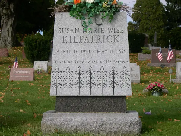 A light grey granite monument with an angled face, the full name and a maiden name, an epitaph line and a row of carved wheat sheaves, on a dark granite base