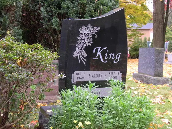 A polished black granite monument with a wave-cut top, the family name in script, a carved floral spray and stacked name tablets