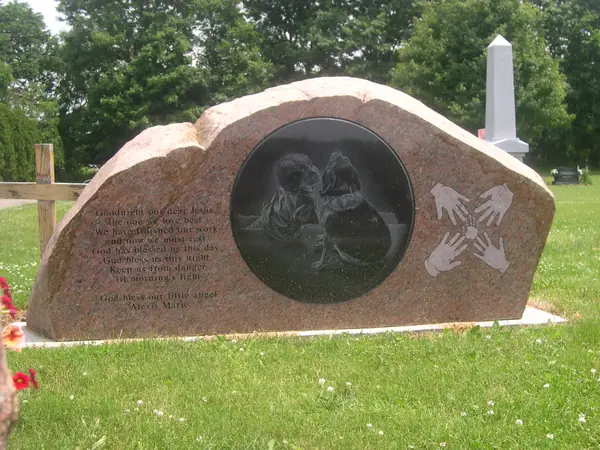 A rose granite boulder-shaped monument with a polished oval panel carrying an etched portrait of two children, carved hands and a verse