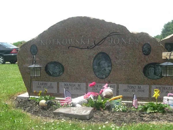 A long rose granite boulder-shaped family monument carrying two surnames and five name panels, each with its own oval etched portrait