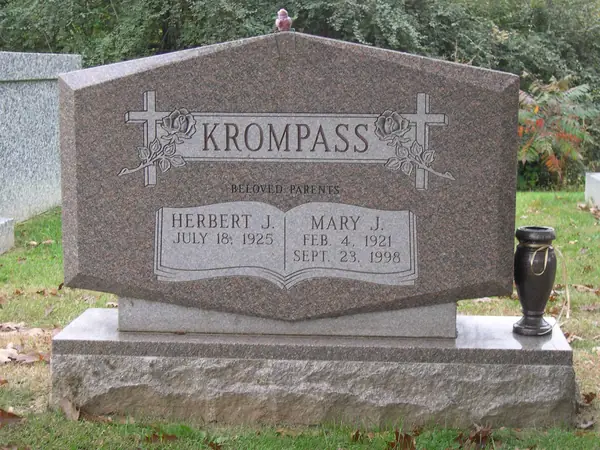 A rose granite monument with a peaked top, carved crosses and roses at both shoulders, a relationship line and two name tablets
