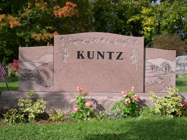 A wide rose granite monument in three sections, the centre carrying the family name and carved florals, the wings etched with countryside scenes