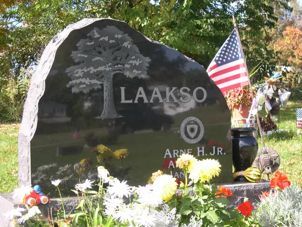 A polished black granite monument with a rough-hewn edge, a carved tree, the family name and a service emblem below