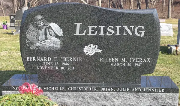 A polished dark granite monument with a wave-cut top, an etched scene of a couple reading, the family name in raised lettering and a marriage emblem