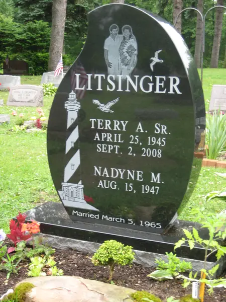 An oval polished black granite monument with an etched couple's portrait, a carved lighthouse and gull, two names and a marriage date across the foot
