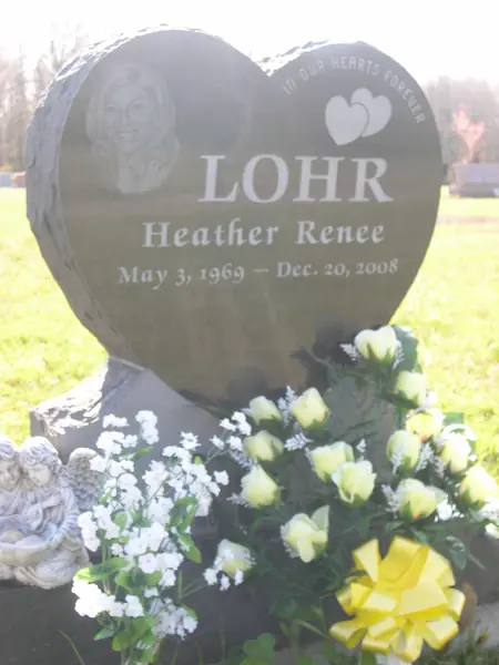 A polished black granite heart-shaped monument with an etched portrait, two carved hearts, a name in script and a single line of dates