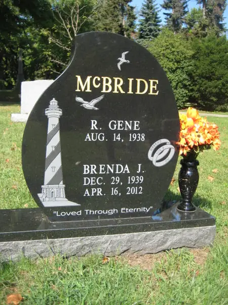 A polished black granite monument with a wave-cut top, the family name in gold lettering, a carved lighthouse and gull, two names and an epitaph