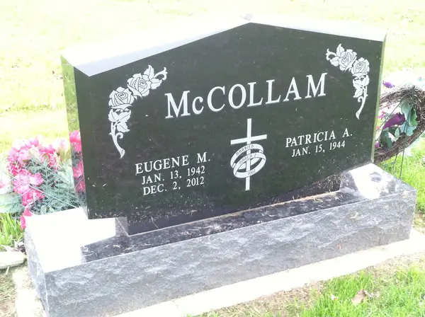 A polished black granite monument with an angled peaked top, roses carved at both corners and a cross with a wheat sheaf between the two names