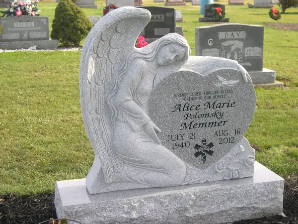 A monument carved as a mourning angel resting on a granite heart, with a name in script, an emergency-services emblem and dates cut into the heart