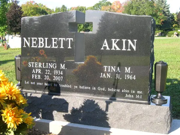 A dark granite double monument carrying two surnames either side of a pierced cross cut through the stone, with a scripture verse below