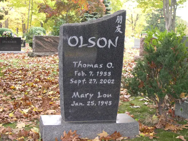 A polished dark granite monument with a wave-cut top, the family name in raised lettering, two names in script and Chinese characters carved at the corner