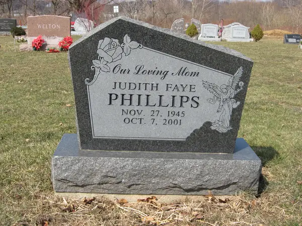 A dark granite monument with an angled peaked top, a rose carved at one corner and an angel at the other, above a relationship line and the full name
