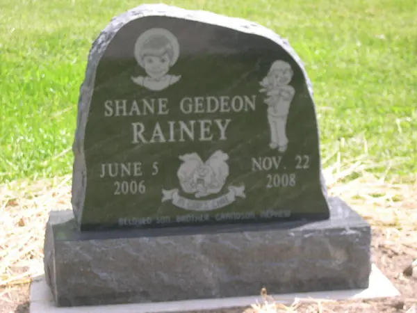 A dark granite monument with a rounded top, etched cherubs at both upper corners and a carved banner between the two dates of a short life