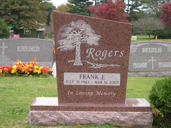 A red granite monument with a wave-cut top, a carved willow tree, the family name in script and a single name tablet with an epitaph